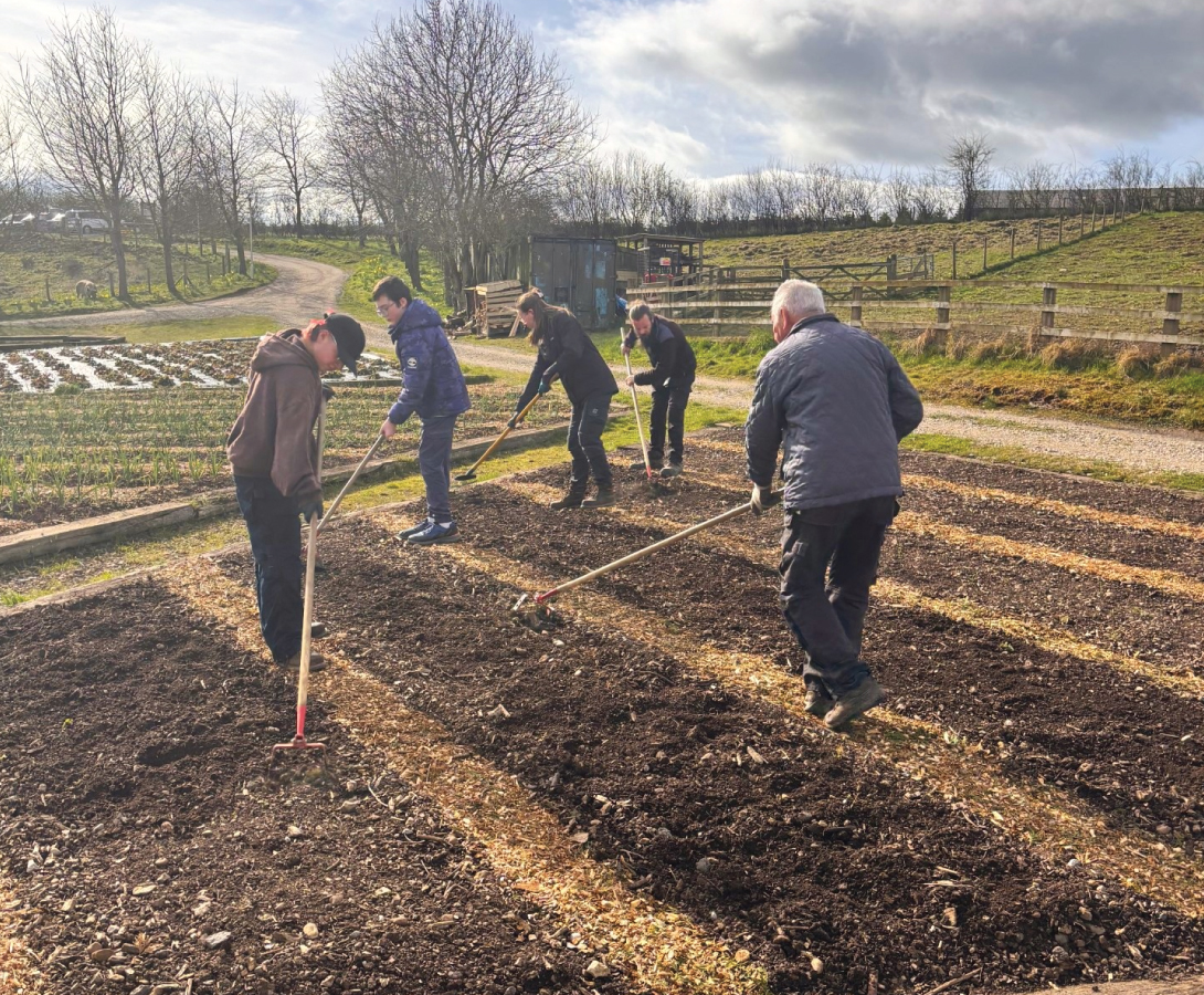 Alfie is stood with staff on the compost, using different horticulture tools to create the bed rows.