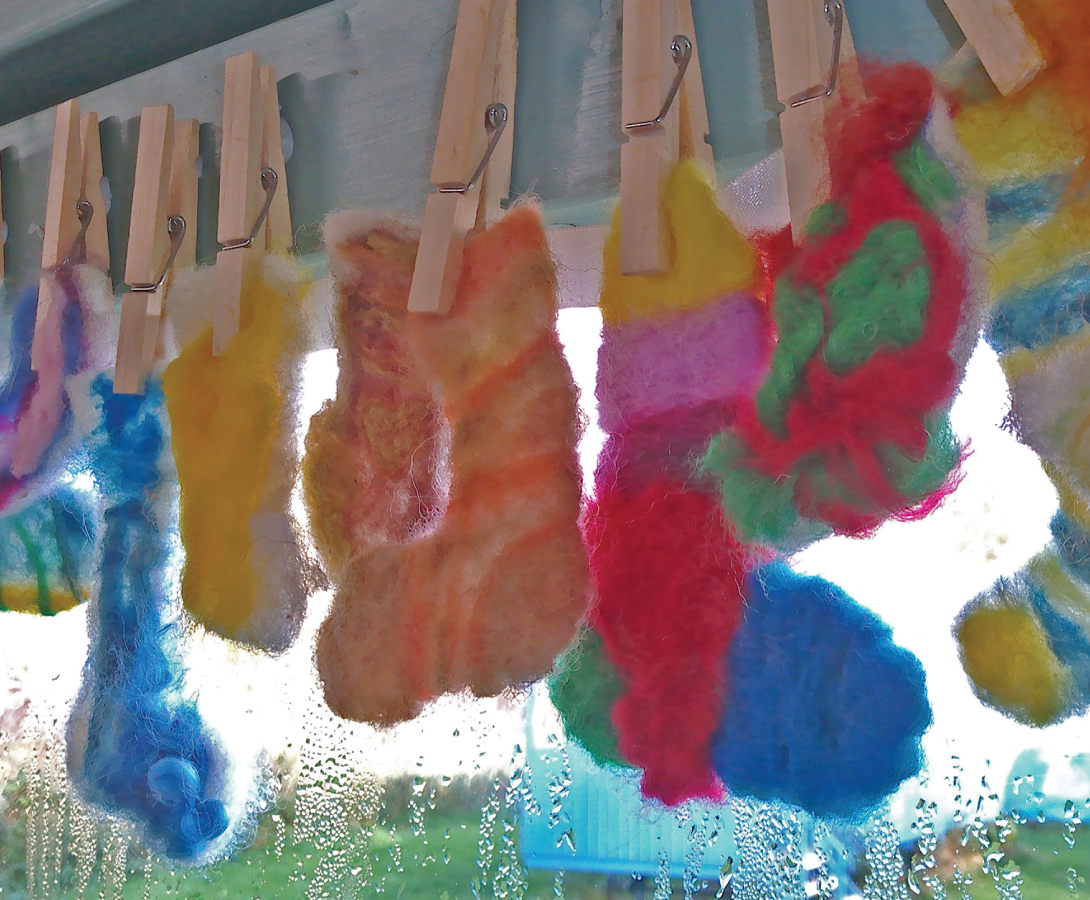 Vibrant felted socks, created by Clervaux Garden School students, are hung on a washing line next to a window to dry.