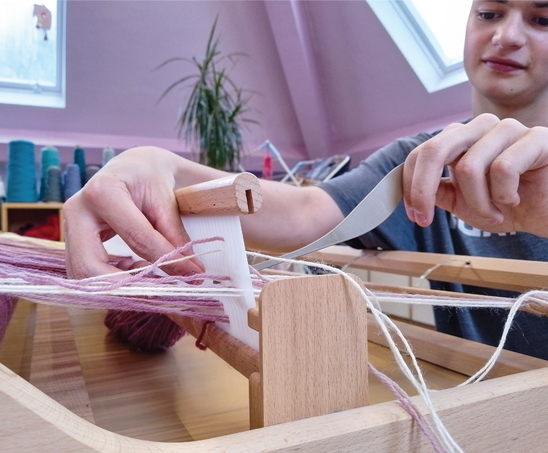 A student of Brantwood school is weaving a blanket on a loom.