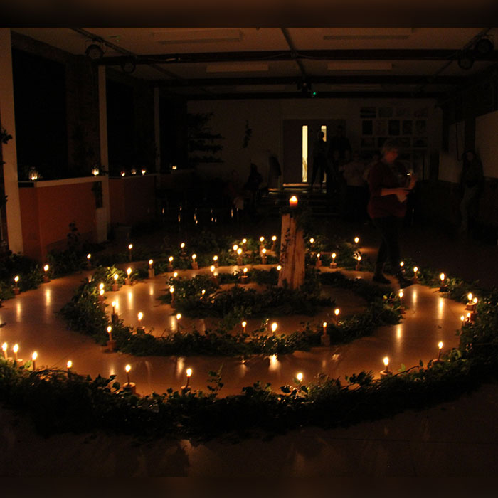 Pictured is someone walking the Advent spiral, with vegetation and lit candles arranged in a spiral, creating a warm glow.