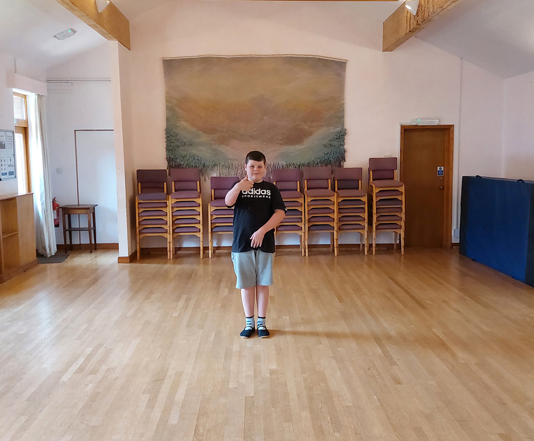 A Grace Garden student performs his Eurythmy sequence, inspired by a daisy, in the hall. The thumbs-up in the image confirms that he is ready.