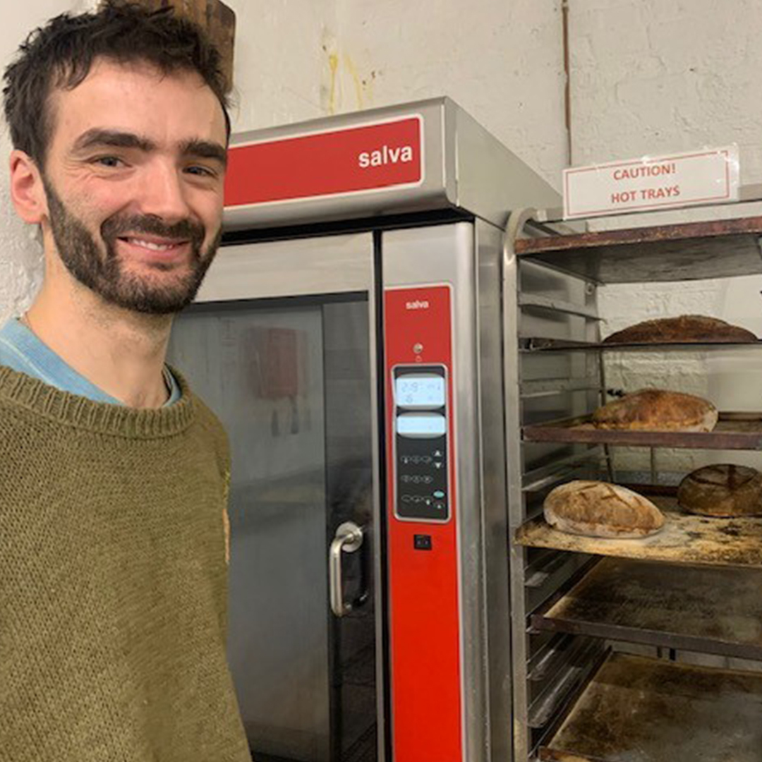 A staff member is pictured proudly in the kitchen, standing in front of the sourdough the staff made during their nutrition course.